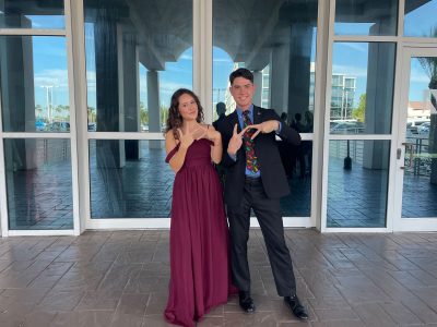 Two people dressed in fancy clothes flashing "VT" signs with their fingers.